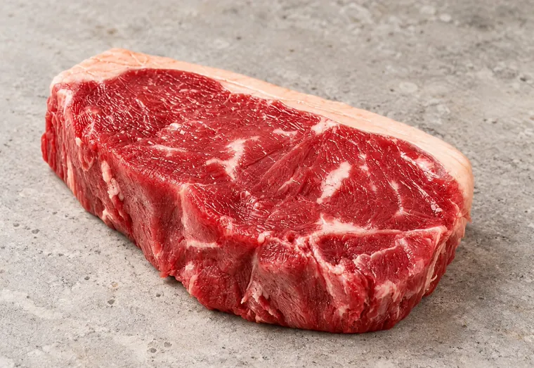 Bife alto de contrafilé cru, com a capa de gordura.