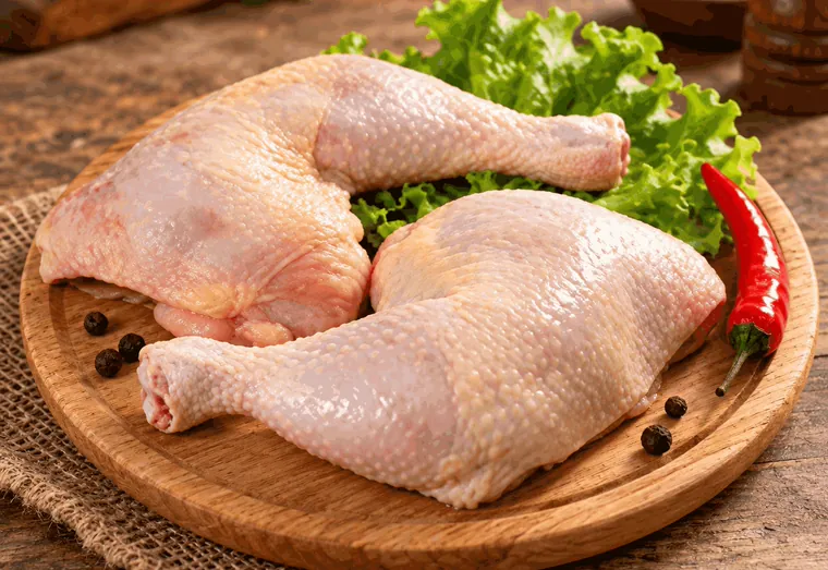 Duas coxas com sobrecoxa de frango cruas sobre tábua redonda, com alface.