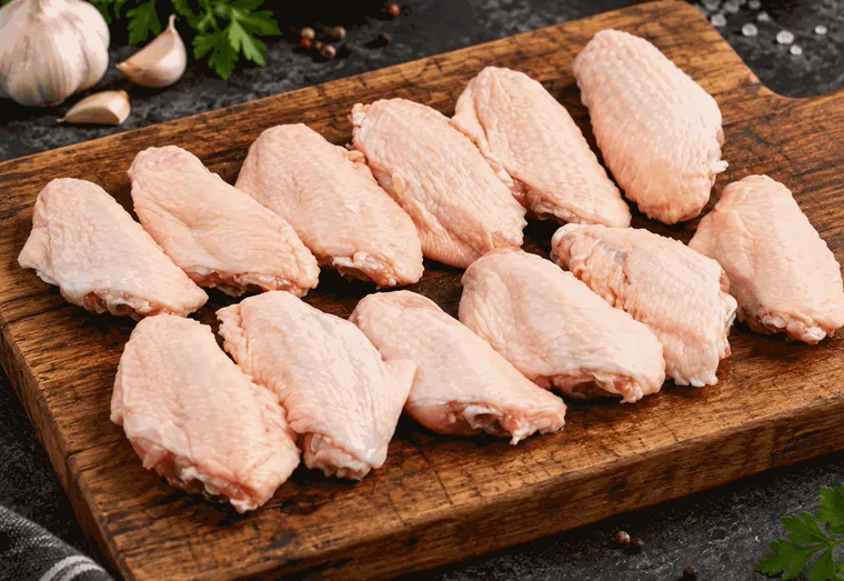 Meios da asa de frango crus, sem tempero, sobre tábua de madeira.