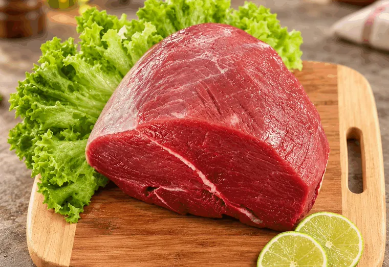 Peça de patinho crua sobre tábua, com alface e rodelas de limão.