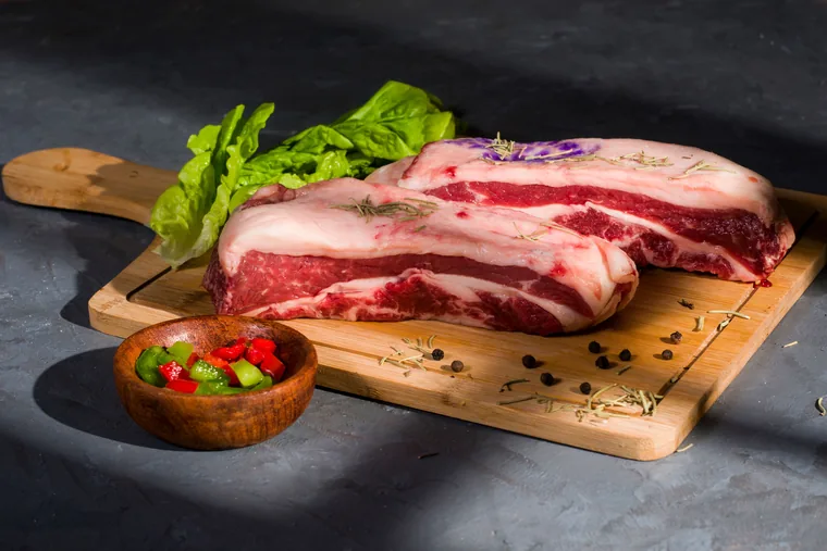 Peça de costela bovina crua sobre tábua de madeira.