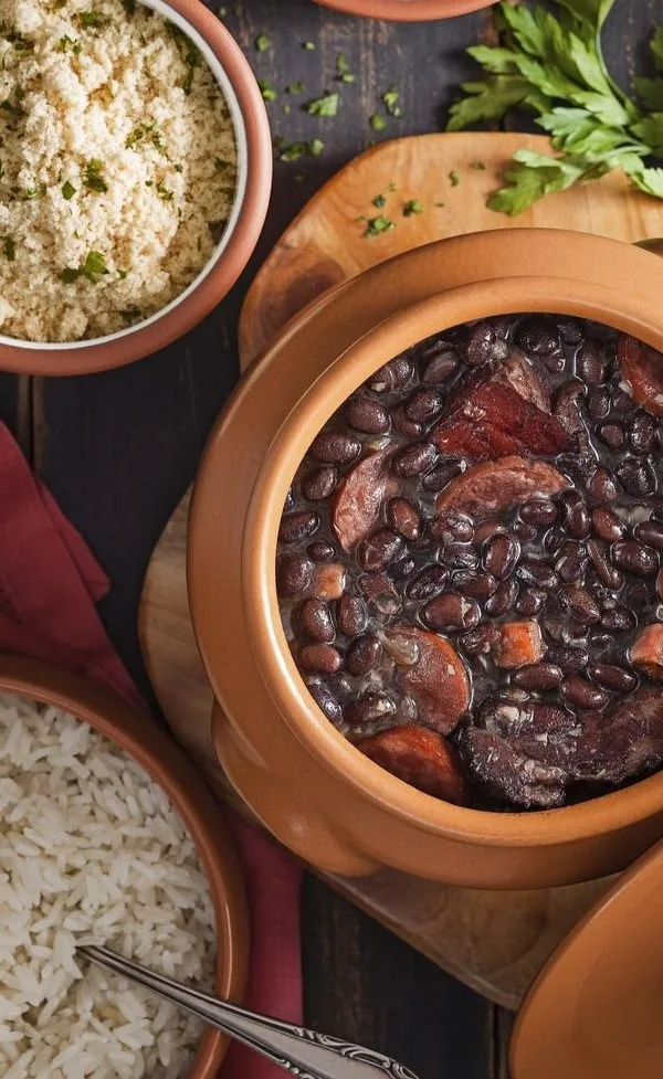 Feijoada servida em panela de barro com arroz e farofa.